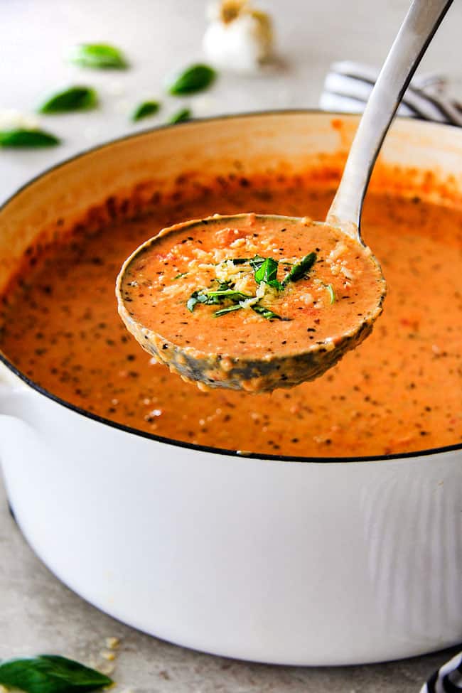 This Tomato Basil Soup recipe is our family favorite! Its super easy without any chopping! bursting with flavor and I love the addition of Parmesan! serving creamy tomato basil soup with a silver ladle.