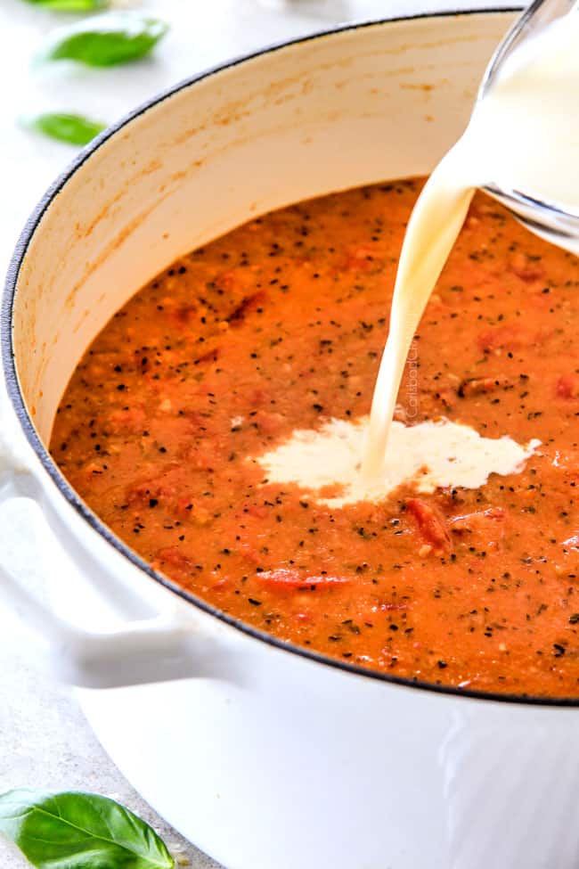 This Tomato Basil Soup recipe is our family favorite! Its super easy without any chopping! bursting with flavor and I love the addition of Parmesan! showing how to make tomato basil soup by adding cream to a large pot of tomato soup