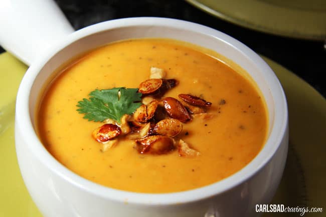 Mega creamy (WITHOUT any cream), Thai Butternut Squash, Sweet Potato, Carrot Soup infused with red curry, ginger, garlic coconut milk, and sriracha - the layers of flavor are SO comforting and positively ADDICTING! side view of Curried Butternut Squash recipe with honey sriracha squash seeds