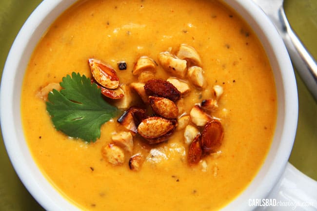 Mega creamy (WITHOUT any cream), Thai Butternut Squash, Sweet Potato, Carrot Soup infused with red curry, ginger, garlic coconut milk, and sriracha - the layers of flavor are SO comforting and positively ADDICTING! top view of curried butternut squash soup with squash seeds, peanuts and cilantro