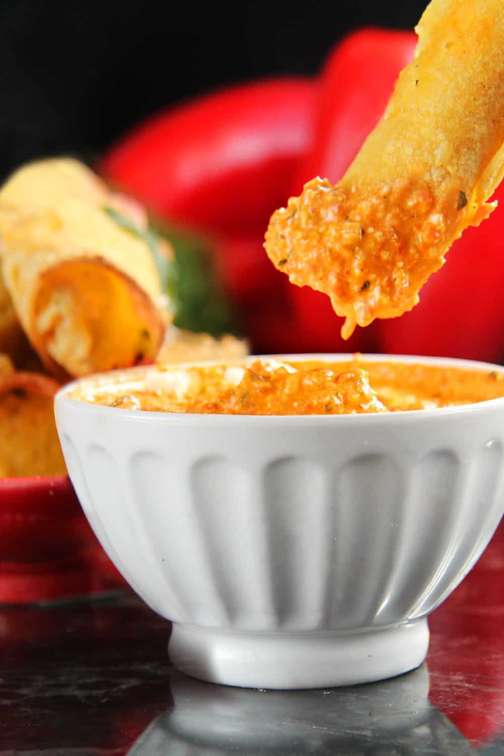 Breakfast Taquitos on a red plate with a close up photo showing the red pepper and feta dipping sauce.