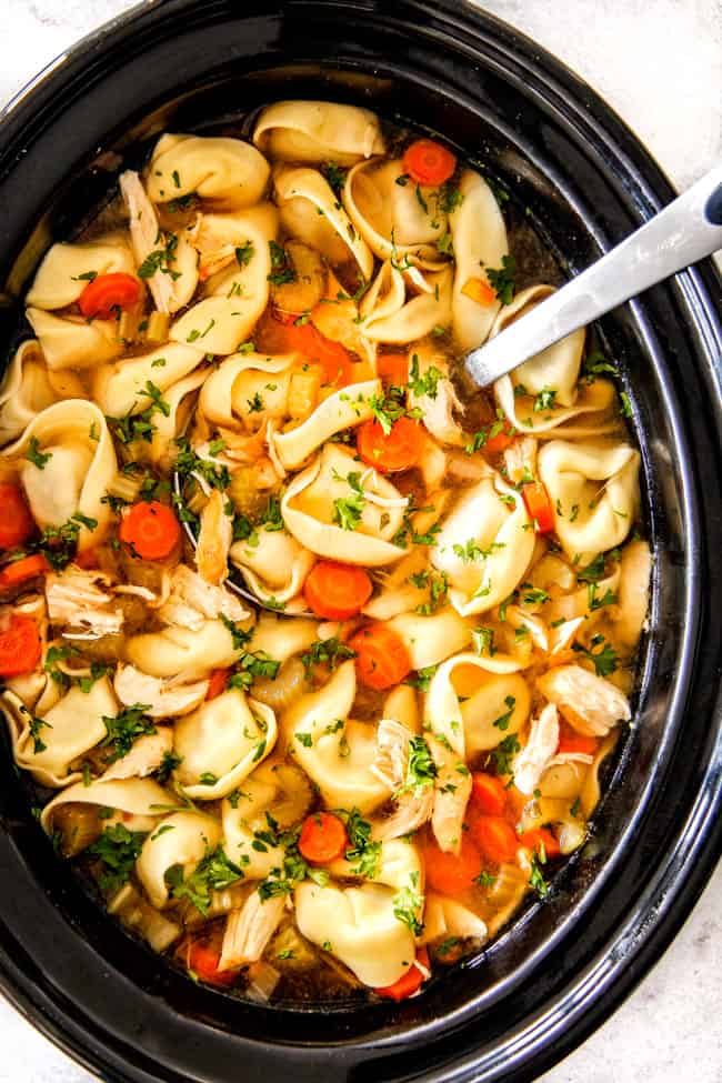 This is the BEST Slow Cooker Chicken Tortellini Soup you will ever try! It's super easy, seasoned to perfection and a comforting, satisfying dinner any night of the week! top view of Chicken Tortellini Soup with cheese tortellini, carrots, celery, onions, garlic and spices in pot