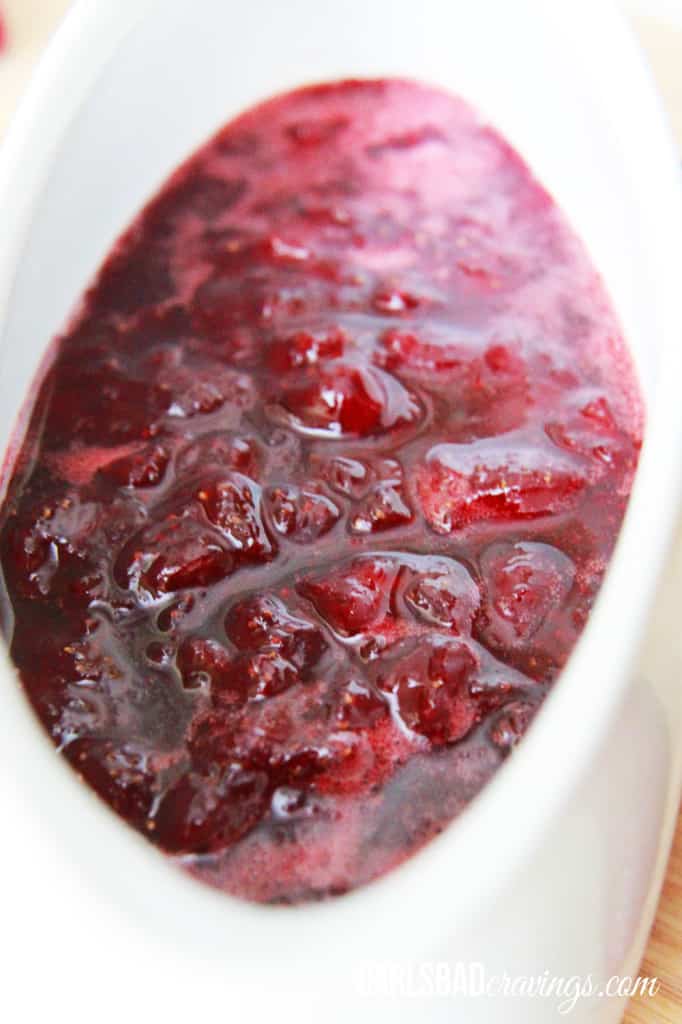 Front angle of home made Strawberry Syrup being poured out of a white bowl over french toast.