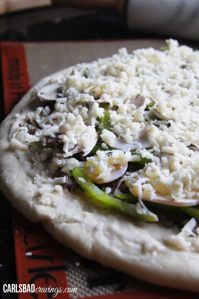 showing how to make Philly Cheesesteak Pizza by layering pizza with mozzarella cheese