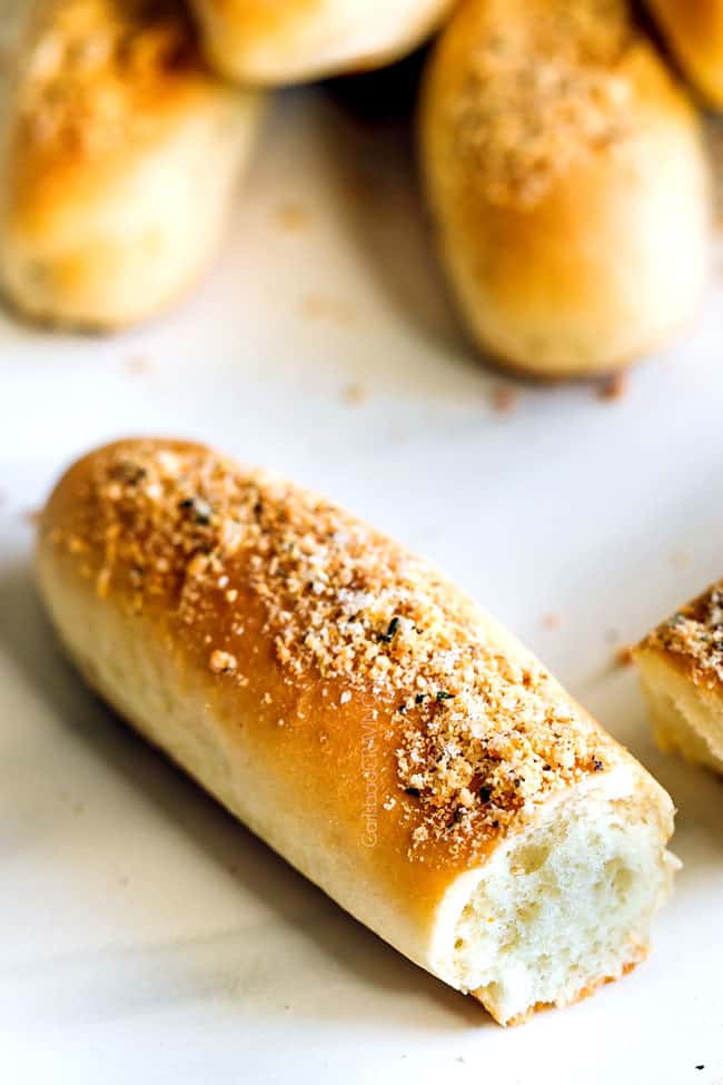a soft, buttery breadstick broken in half laying on a white counter with garlic parmesan seasoning