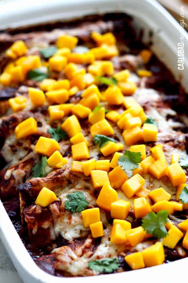 Showing baked Chipotle Chicken Enchiladas with mango in a casserole dish from the front view.