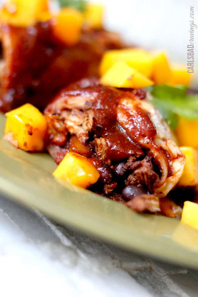 Showing a serving of baked Chipotle Chicken Enchiladas with mango on a green plate.
