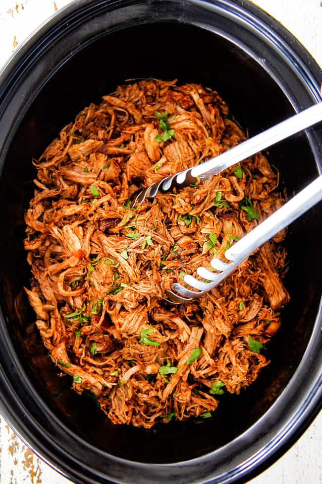 top shot of slow cooker cafe rio sweet pulled pork in crock pot with silver tongs