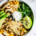 a bowl of easy crockpot chicken tortilla soup garnished with sour cream, avocados, cilantro and tortilla strips