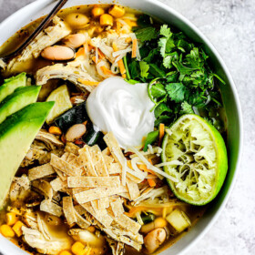 a bowl of easy crockpot chicken tortilla soup garnished with sour cream, avocados, cilantro and tortilla strips