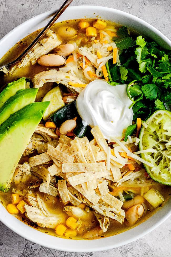 a bowl of slow cooker chicken tortilla soup garnished with sour cream, avocados, cilantro and tortilla strips