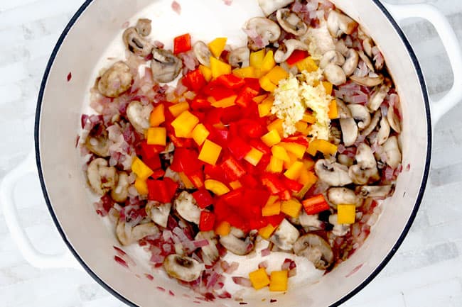 Showing how to make Cajun Chicken Pasta Soup in a white pot adding belle peppers into the mushroom cream sauce.