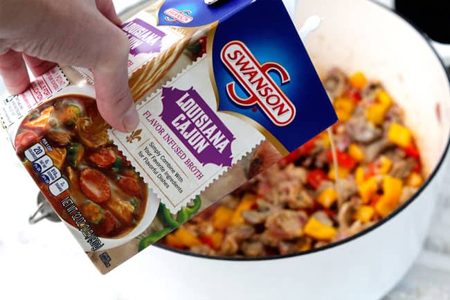Showing how to make Cajun Chicken Pasta Soup in a white pot adding Swanson Louisiana Cajun broth.