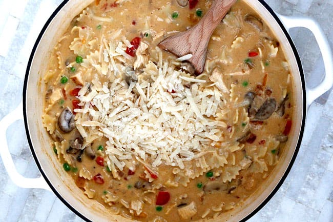 Showing how to make Cajun Chicken Pasta Soup in a white pot adding cheese.