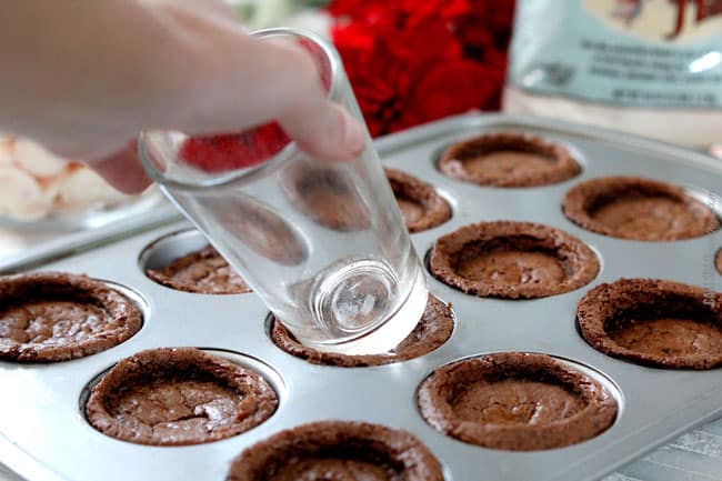 Showing how to make Peppermint Eggnog Brownie Cups by smashing the cookies into cups with a class to create the correct shape.
