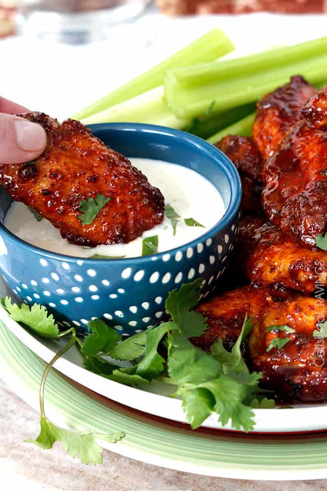 Showing the Honey Buffalo Hot Wings on a plate with celery and dipping a wing into the blue cheese dipping sauce.