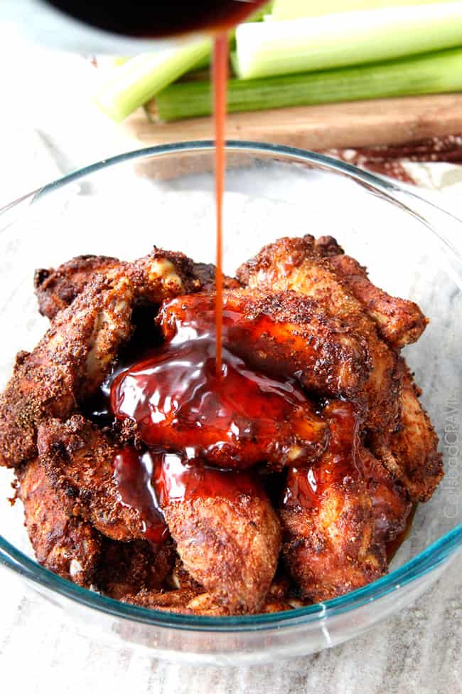 Showing how to make Honey Buffalo Hot Wings by adding the sauce to the baked wings in a clear bowl.