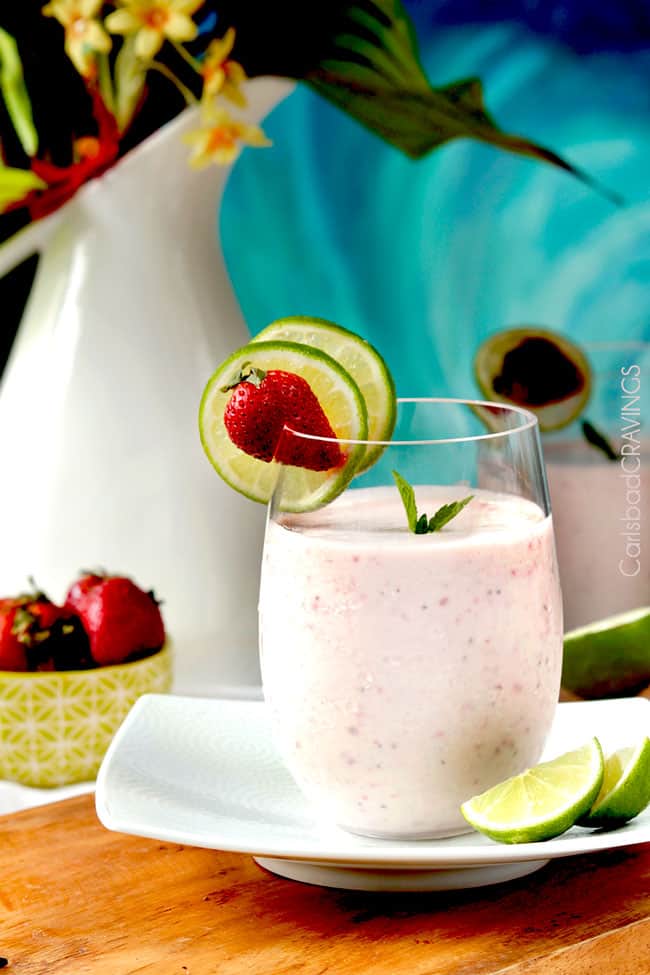 a glass of strawberry banana protein smoothie garnished with lime wedges and berries