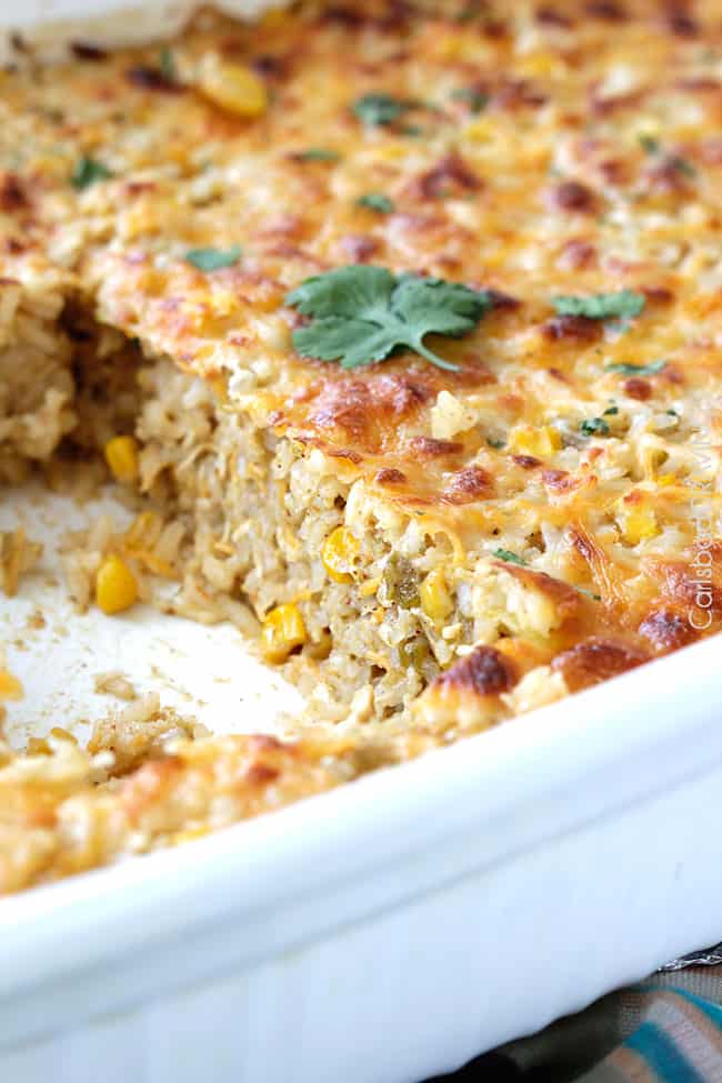 Side angle of Salsa Verde Honey Lime Chicken rice with cheese on top in a white casserole dish showing the layers.