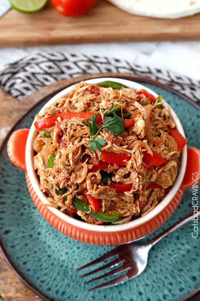 Crockpot Chicken Fajitas are the easiest way to make restaurant delicious chicken fajitas at home! Dump and simmer while you take a nap and let the citrus fiesta bath tenderize your chicken. top view of crockpot chicken fajitas with cilantro garnish in an orange serving bowl