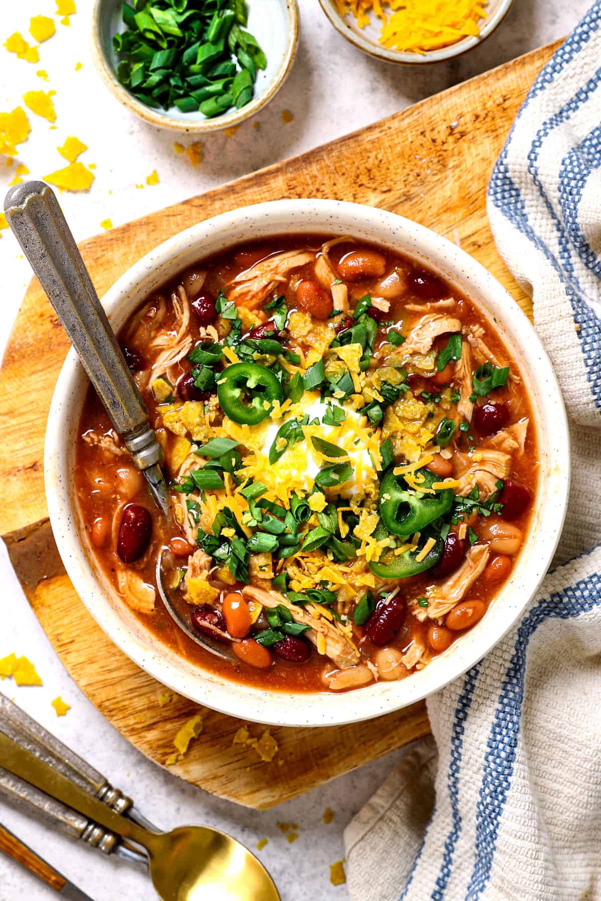 overhead view of bowl of chicken chili recipe garnished with tortilla strips and shredded cheese