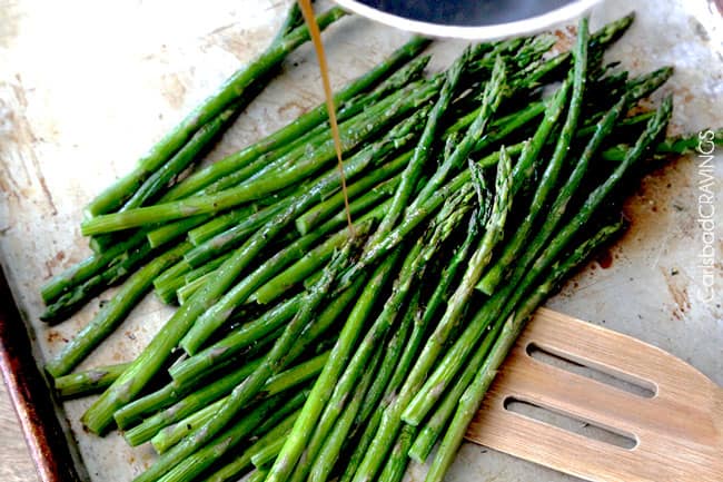 overhead view of showing how to make balsamic asparagus with asparagus on baking sheet with spatula