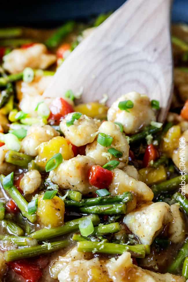 Side view of Honey Lemon Chicken Stir Fry over white rice in a bowl mixing with a wood spoon..