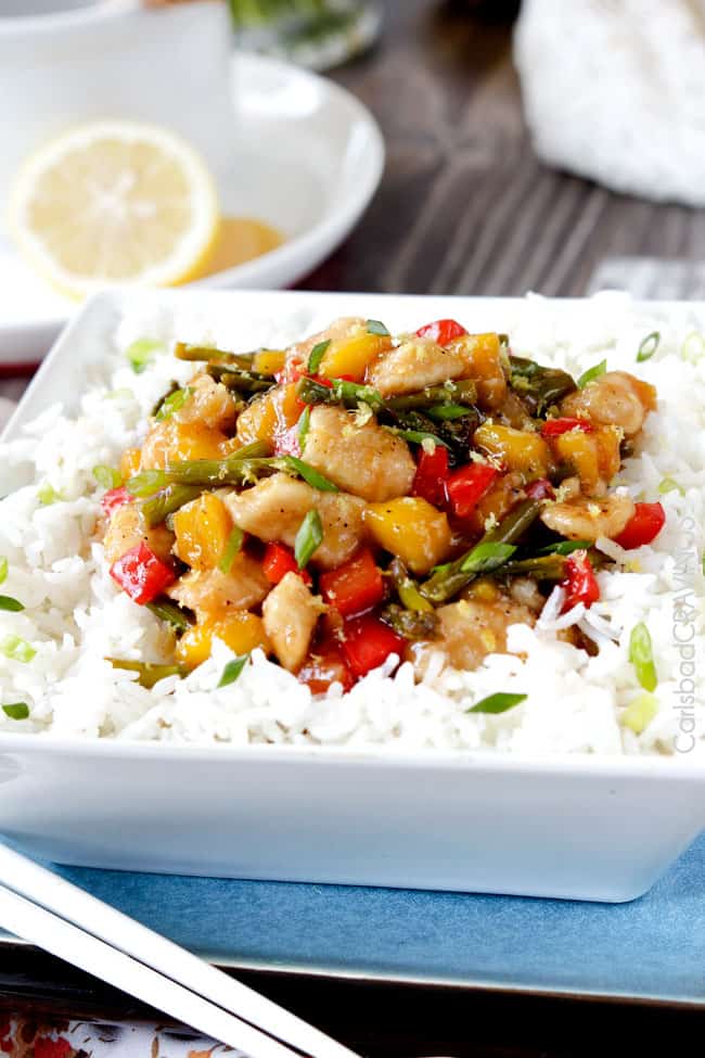 Side view of Honey Lemon Chicken Stir Fry over white rice in a bowl with mango and belle peppers on top. .