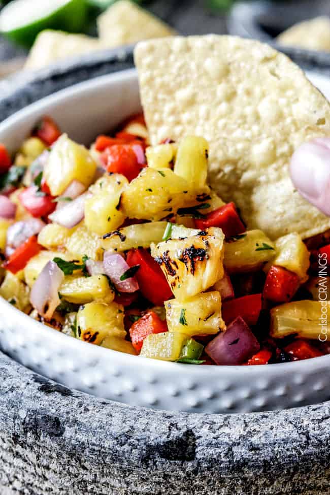 Home made Pineapple Salsa with a corn chip being dipped in the white bowl.