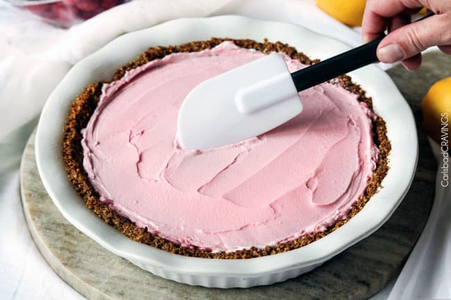 Showing how to make Frozen Lemon Meringue Pie by smoothing out the ingredient in the pie crust.