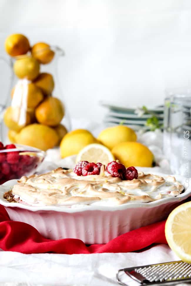 A full Frozen Lemon Meringue Pie in a white pie pan with raspberries and lemons on the side.