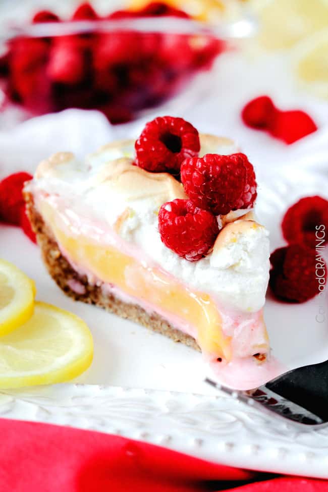 A single slice of Frozen Lemon Meringue Pie on a white plate with raspberries and a fork.