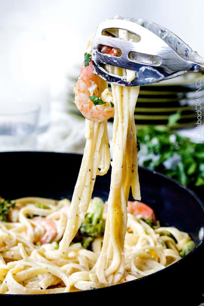 Shrimp Fettuccine Alfredo smothered in a velvety, creamy Alfredo sauce that's lightened up but tastes every bit as decadent as the finest restaurant Alfredo without any of the guilt or the price! This Roasted Shrimp Fettuccine Alfredo Recipe is bursting with juicy oven roasted shrimp. two tongs picking up Shrimp Fettuccine Alfredo with broccoli