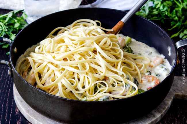Shrimp Fettuccine Alfredo smothered in a velvety, creamy Alfredo sauce that's lightened up but tastes every bit as decadent as the finest restaurant Alfredo without any of the guilt or the price! This Roasted Shrimp Fettuccine Alfredo Recipe is bursting with juicy oven roasted shrimp. showing how to make Shrimp Fettuccine Alfredo by adding fettuccine to Alfredo sauce