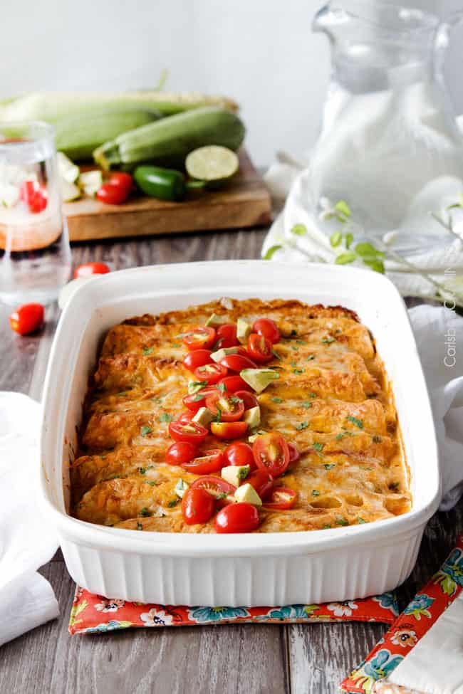 Cheesy Chicken Enchiladas stuffed with tender chicken, cheese and doused in the most irresistible creamy jalapeno sour cream sauce that you will go crazy for! front view of cheesy sour cream chicken enchiladas in white casserole dish with tomatoes and cilantro on top