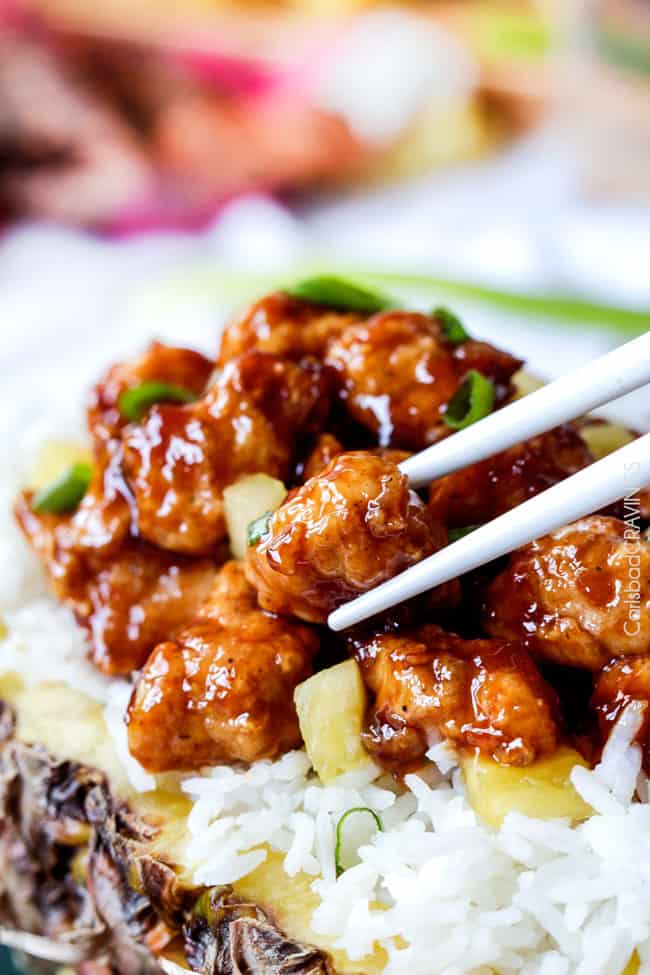 picking up baked Chinese Pineapple Chicken with chopsticks in a delicious pineapple sauce with white rice.