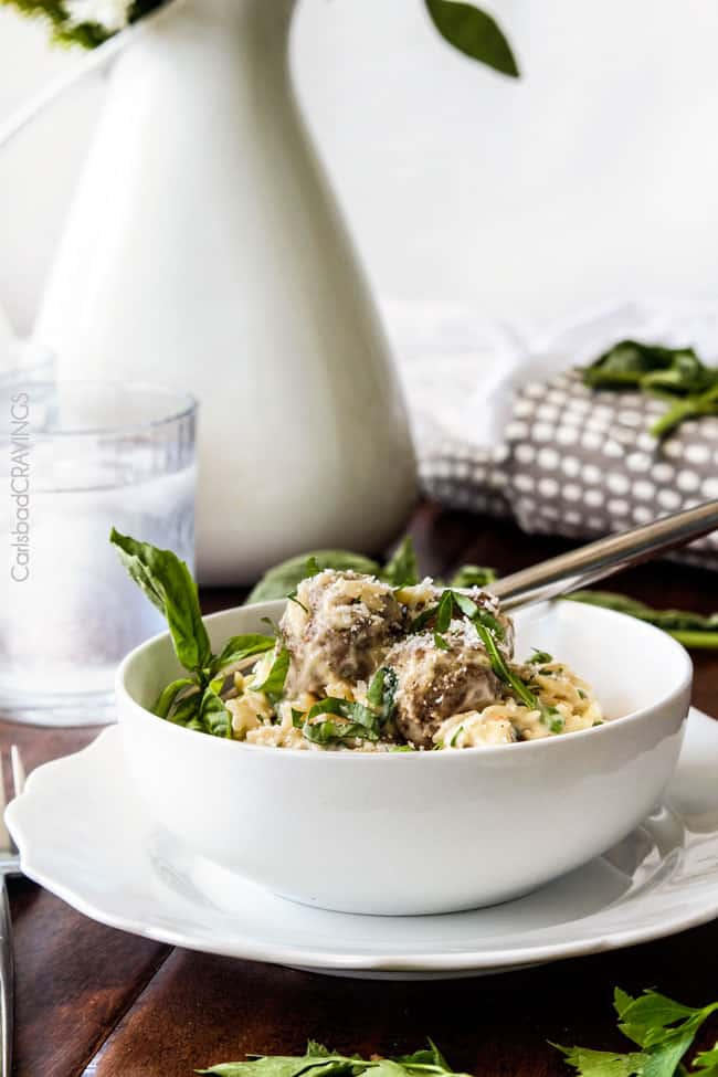 Parmesan Meatballs in a cream sauce with orzo and basil being served in a white bowl.