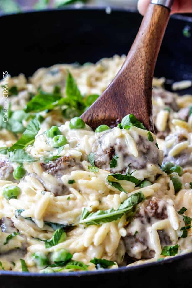 Close uo shot stirring Parmesan Meatballs in a cream sauce with orzo and basil.