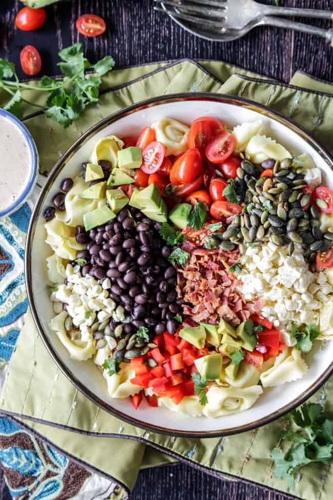 Make ahead, favorite potluck Southwest Pepper Jack Tortellini Salad = cheesy pillows of tortellini, sweet corn, black beans, avocado, bell peppers, etc. bathed in Creamy Salsa Dressing and garnished with bacon, Pepper Jack, sunflower seeds. Oh my YUM! #tortellini #pastasalad #southwest #salad