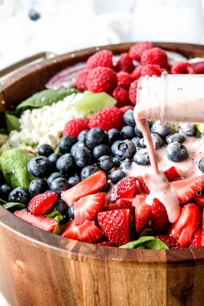 strawberry poppyseed dressing being poured onto a large bowl of spinach berry salad