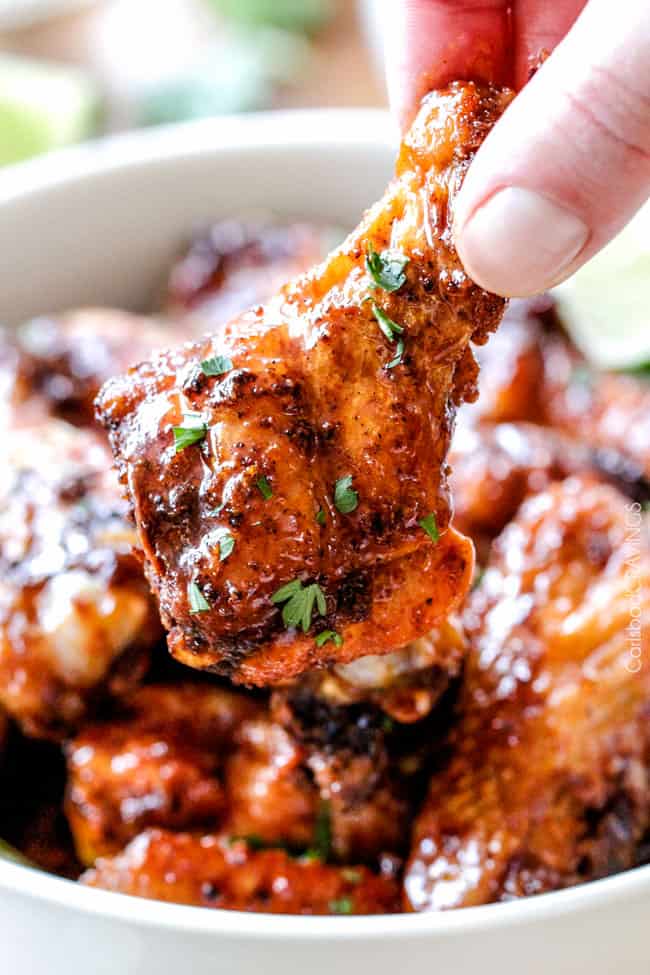 Close up of a single Baked Chipotle Honey Lime Hot Wing held near a bowl of wings.