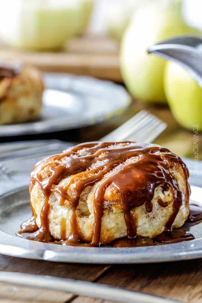 Caramel Apple Dumplings AKA the best apple dumplings ever! Perfectly buttery, flaky pastry, oozing cinnamon and sugar peanut butter filling all drizzled with silky caramel. front view of amish apple dumplings on a silver plate with caramel
