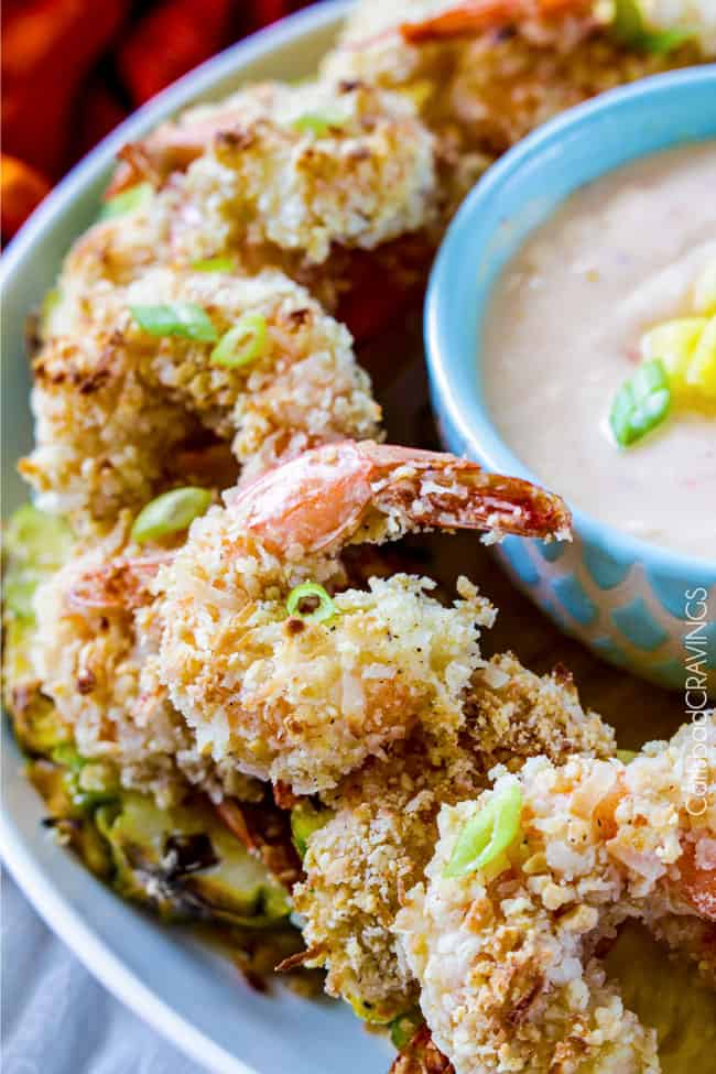 Close up of Coconut Shrimp on a platter next to dipping sauce and green onions on top.