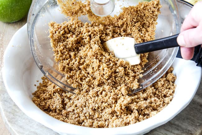 pecan crust mixture being poured into a white pie plate
