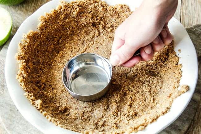 pecan pie crust being pressing into a pie plate with a measuring cup