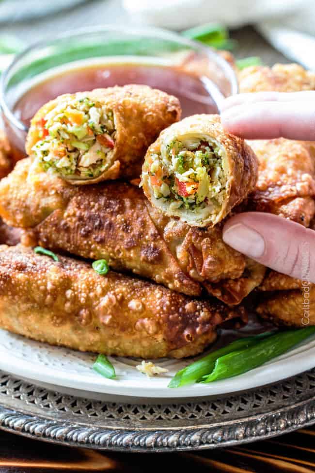 Sweet and Sour Chicken Egg are the best egg rolls I’ve ever had with the best sweet and sour sauce! And made extra fast with the food processor. I am bringing these to all my holiday parties! #appetizer #NewYears #Christmas up close of a hand picking up a Chinese chicken egg roll