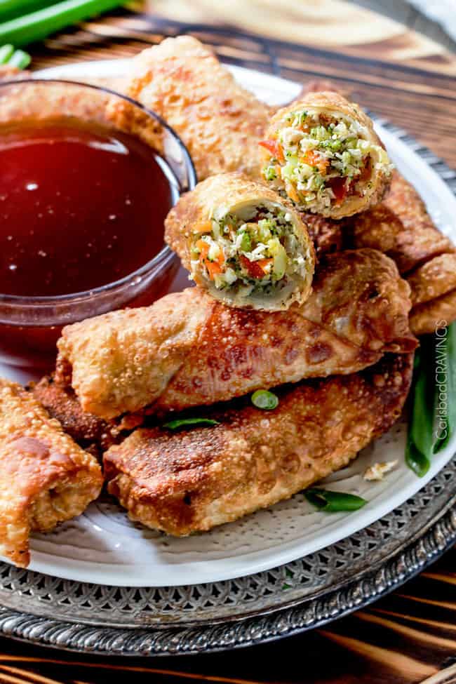 Sweet and Sour Chicken Egg are the best egg rolls I’ve ever had with the best sweet and sour sauce! And made extra fast with the food processor. I am bringing these to all my holiday parties! #appetizer #NewYears #Christmas a pile of homemade chicken egg rolls on a plate with one cut open with the chicken filling spilling outt