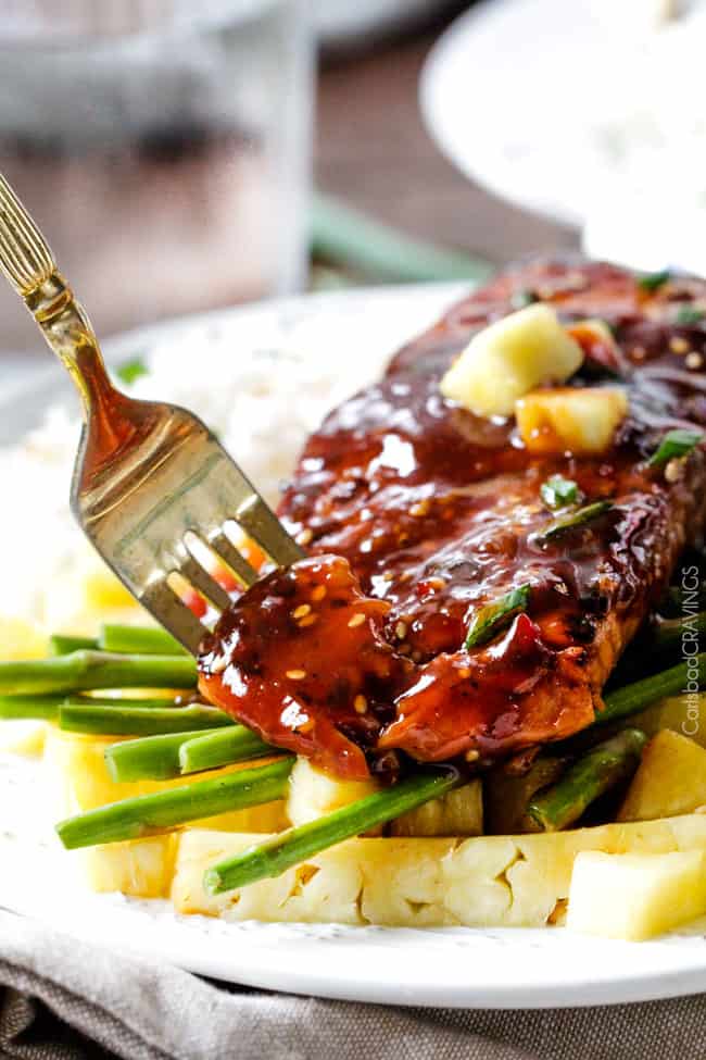 A bite of Asian BBQ Salmon on a plate with asparagus and rice with a piece on a fork.