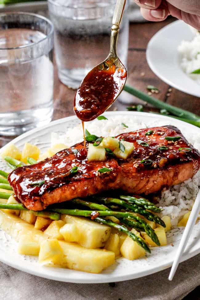 Asian BBQ Salmon on a plate with asparagus and rice with sauce being poured over top. .