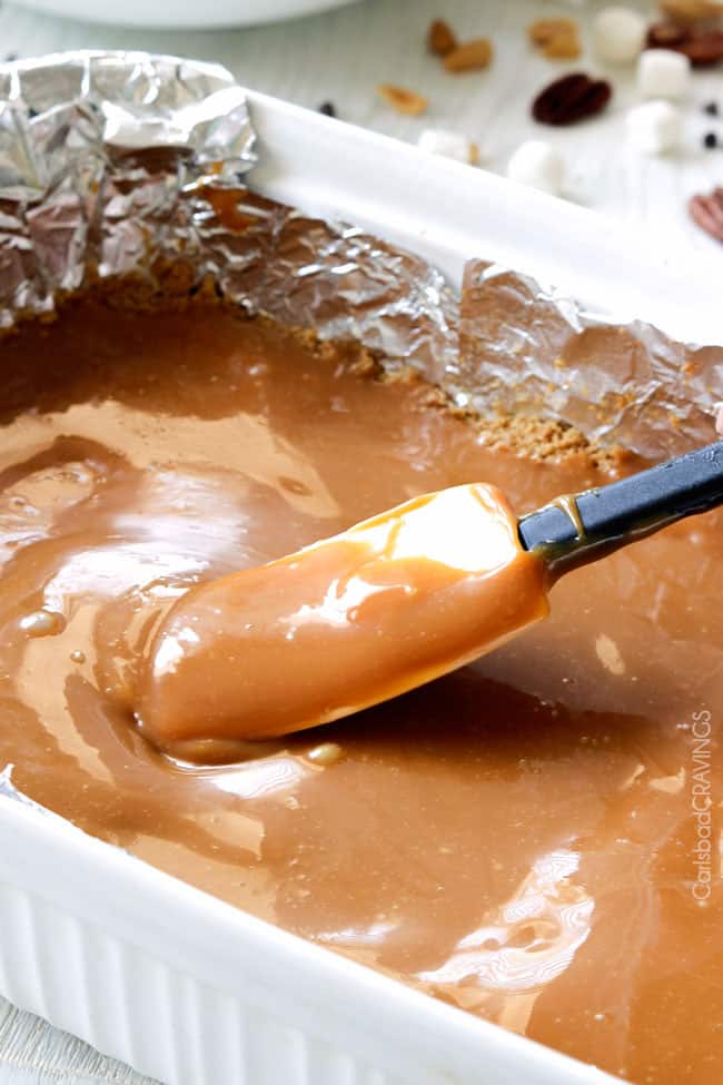 Showing how to make Caramel Nut S'mores Bars smoothing out caramel sauce.